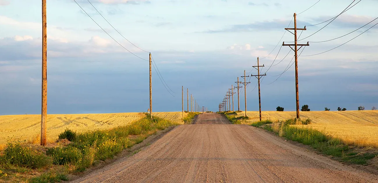 Road through rolling hills and prairie, at sunset with power lines on both sides.